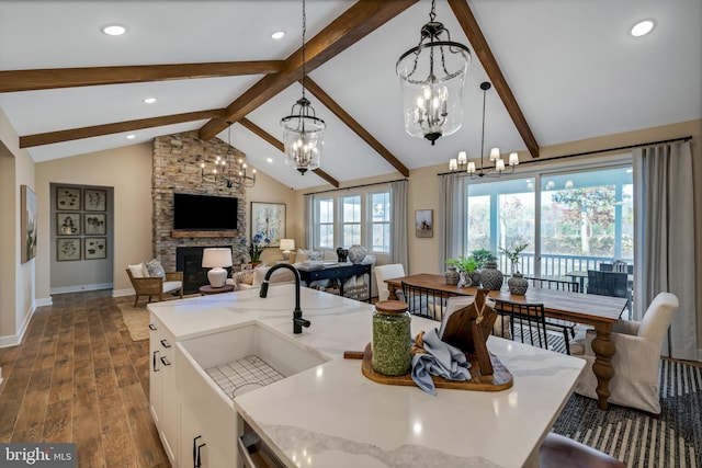 kitchen featuring dark hardwood / wood-style flooring, decorative light fixtures, a fireplace, vaulted ceiling with beams, and an island with sink