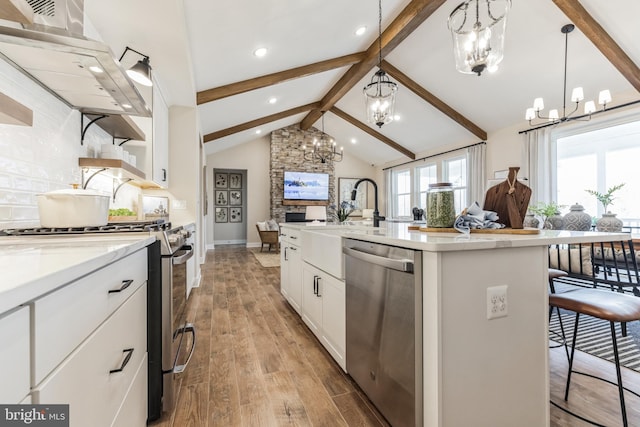 kitchen featuring pendant lighting, a kitchen island with sink, white cabinets, stainless steel dishwasher, and range hood