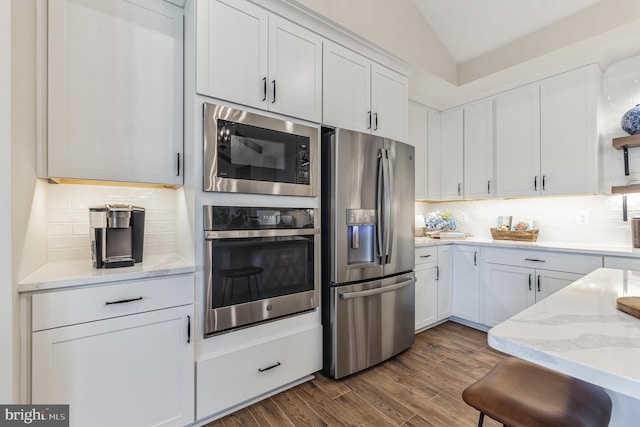 kitchen featuring dark hardwood / wood-style flooring, backsplash, stainless steel appliances, vaulted ceiling, and white cabinetry