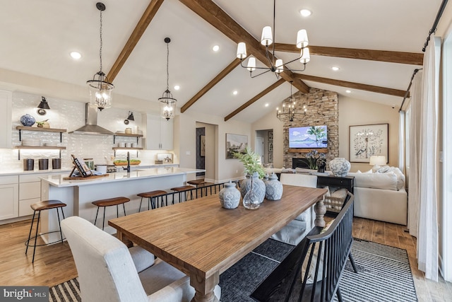 dining room featuring beamed ceiling, light wood-type flooring, a fireplace, and high vaulted ceiling