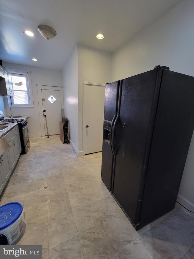 kitchen with gas range oven, white cabinets, and black refrigerator with ice dispenser