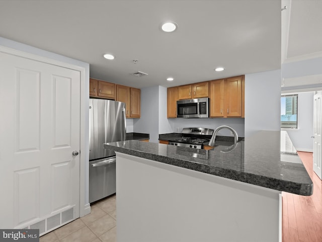 kitchen with stainless steel appliances, dark stone counters, and light tile patterned floors