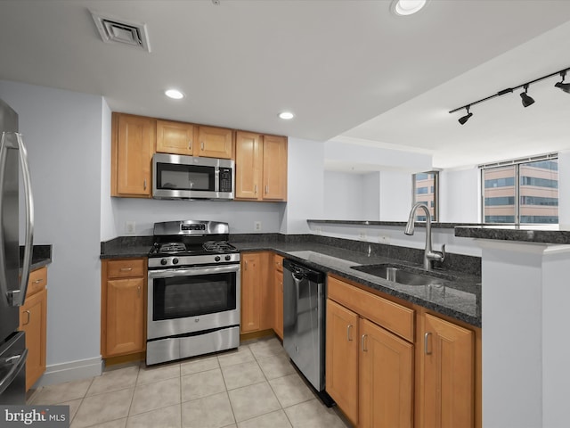 kitchen with stainless steel appliances, track lighting, light tile patterned floors, dark stone countertops, and sink