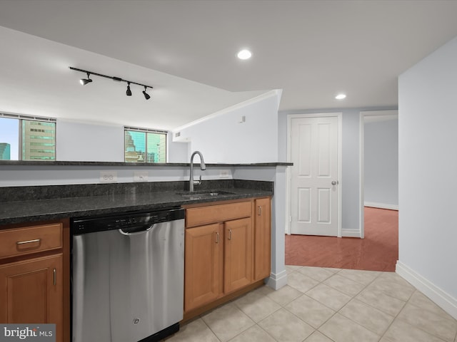 kitchen with dishwasher, dark stone countertops, rail lighting, sink, and light tile patterned flooring