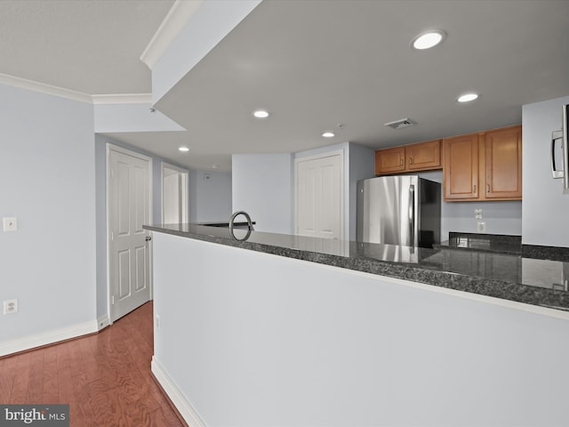 kitchen with ornamental molding, kitchen peninsula, wood-type flooring, stainless steel refrigerator, and dark stone counters