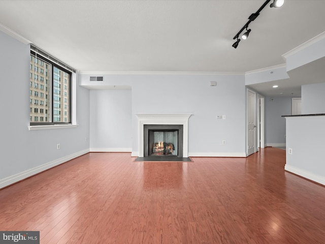 unfurnished living room featuring hardwood / wood-style floors, crown molding, and rail lighting