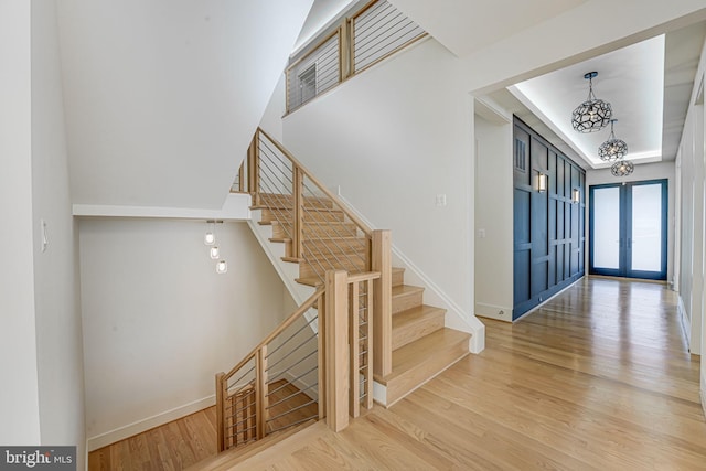 staircase with french doors, wood-type flooring, and an inviting chandelier