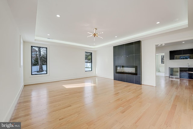 unfurnished living room with a tiled fireplace, beverage cooler, a raised ceiling, and light hardwood / wood-style flooring