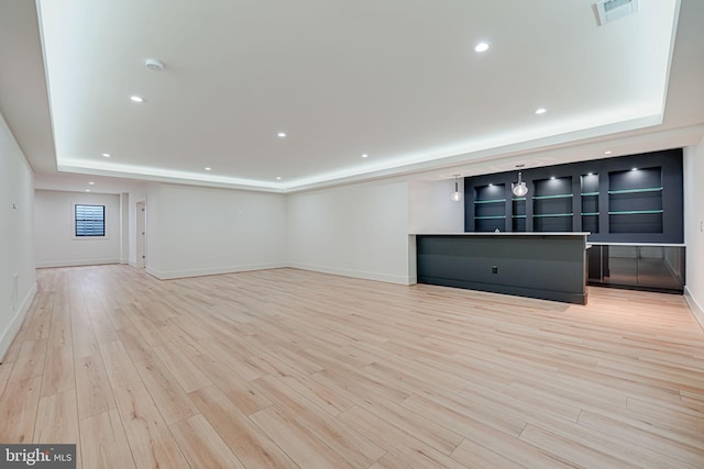 unfurnished living room featuring a raised ceiling and light hardwood / wood-style flooring