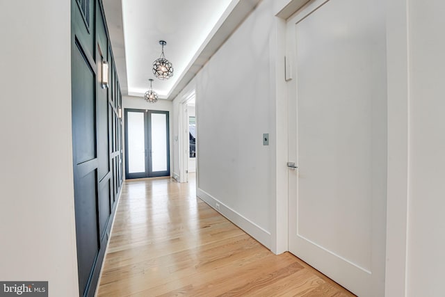 interior space with a chandelier, light hardwood / wood-style flooring, french doors, and a raised ceiling