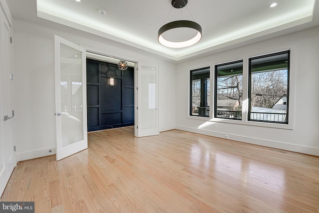 spare room with a tray ceiling and light hardwood / wood-style floors