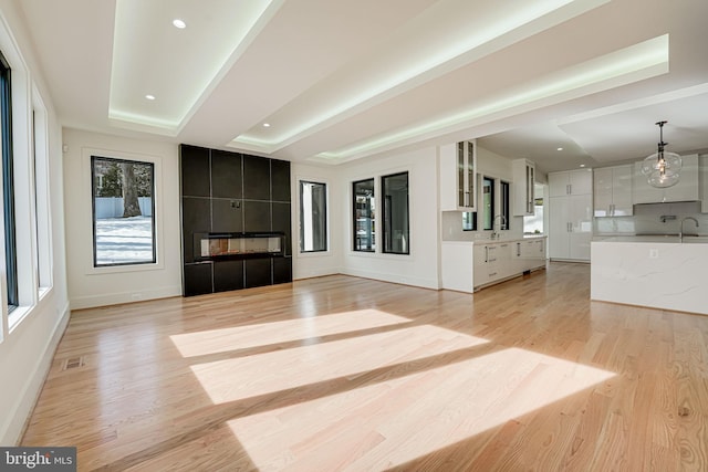 unfurnished living room featuring a tiled fireplace, sink, light hardwood / wood-style floors, and a raised ceiling