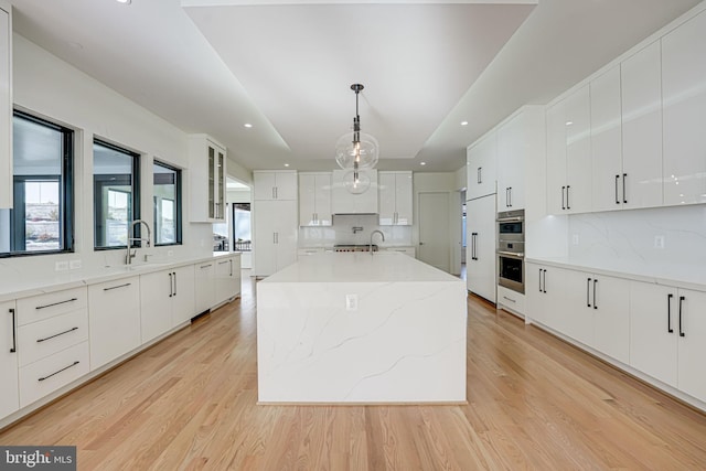 kitchen featuring white cabinetry, hanging light fixtures, a kitchen island, and light wood-type flooring