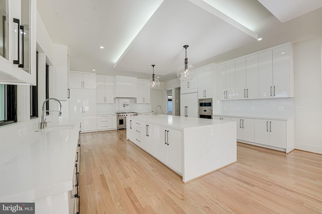 kitchen with a large island, sink, pendant lighting, high quality appliances, and white cabinets