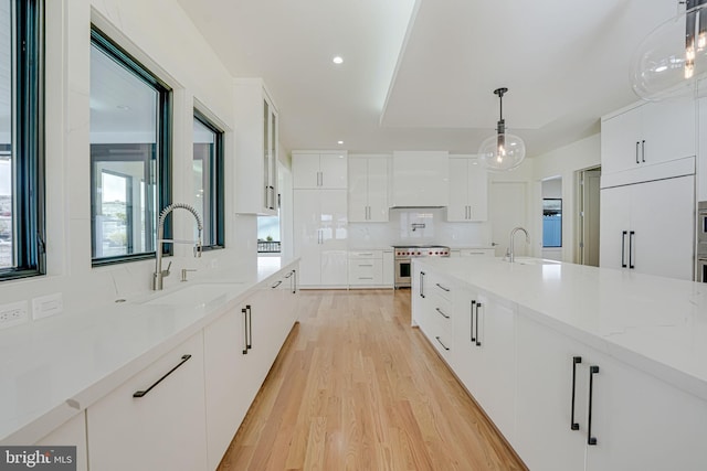 kitchen with pendant lighting, sink, white cabinets, custom exhaust hood, and high end stainless steel range oven