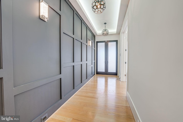 hall with french doors, a tray ceiling, and light hardwood / wood-style floors