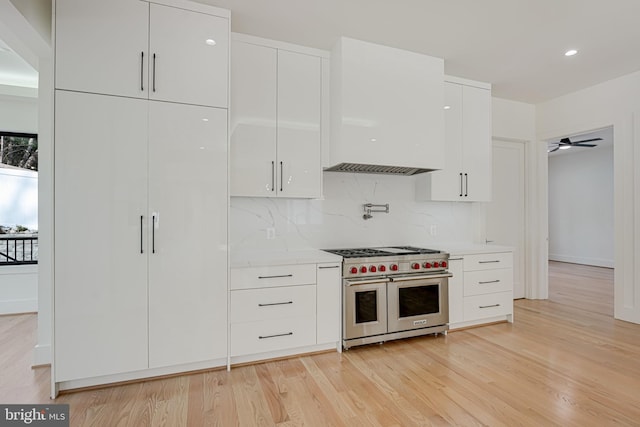 kitchen featuring tasteful backsplash, light wood-type flooring, white cabinets, and range with two ovens