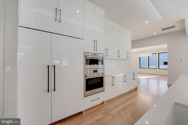 kitchen with paneled built in refrigerator, white cabinets, double oven, and light hardwood / wood-style flooring