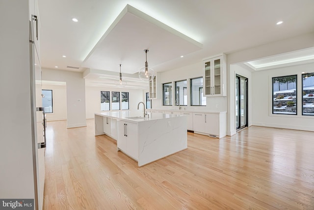 kitchen featuring pendant lighting, sink, white cabinets, a large island with sink, and light wood-type flooring