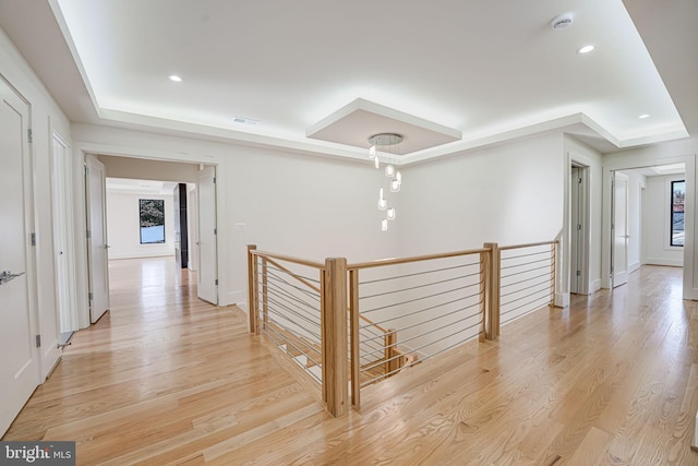 corridor with a raised ceiling, light hardwood / wood-style floors, and a wealth of natural light