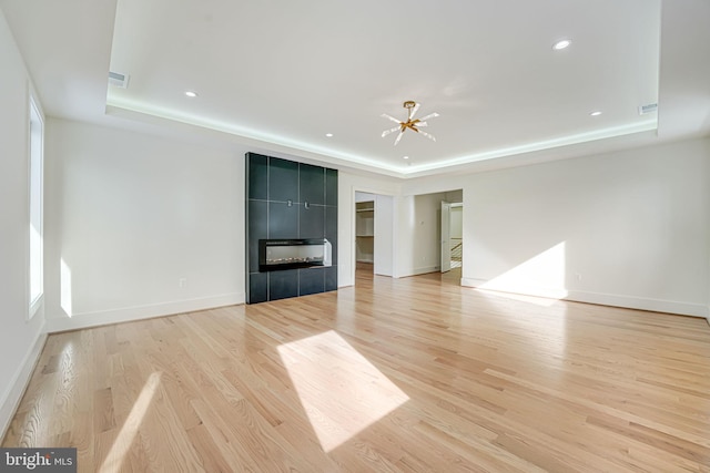 unfurnished living room with a tiled fireplace, a raised ceiling, and light hardwood / wood-style floors