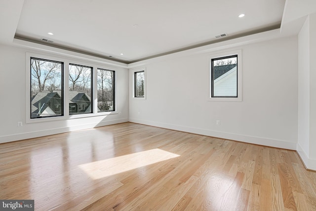 empty room featuring a tray ceiling and light hardwood / wood-style floors