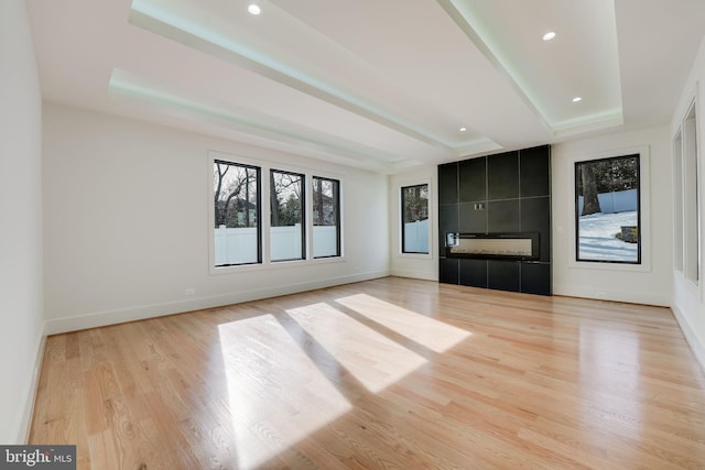 unfurnished living room with a tiled fireplace, light hardwood / wood-style floors, and a raised ceiling