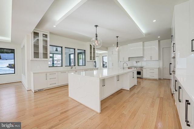 kitchen with pendant lighting, light hardwood / wood-style flooring, a breakfast bar area, white cabinets, and a large island with sink