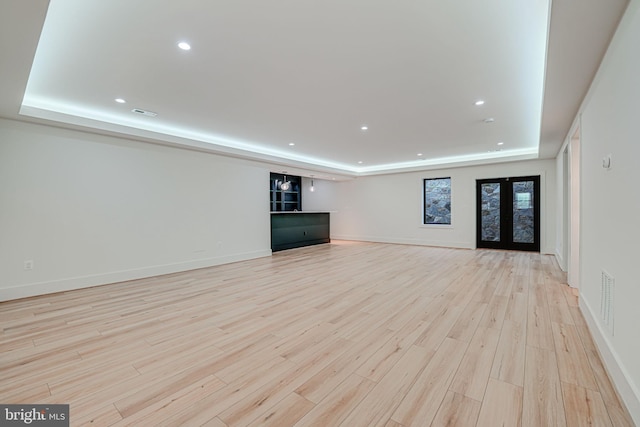 unfurnished living room featuring a tray ceiling, french doors, and light wood-type flooring