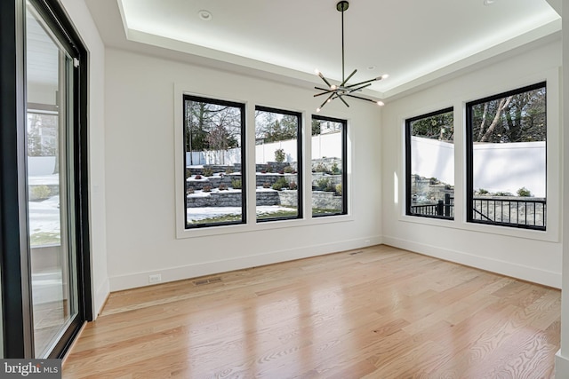 empty room with a notable chandelier, a tray ceiling, and light hardwood / wood-style flooring