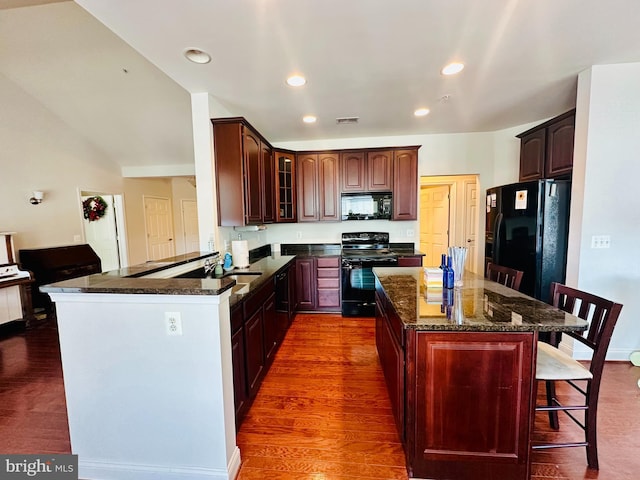 kitchen with black appliances, a kitchen breakfast bar, sink, dark hardwood / wood-style floors, and kitchen peninsula