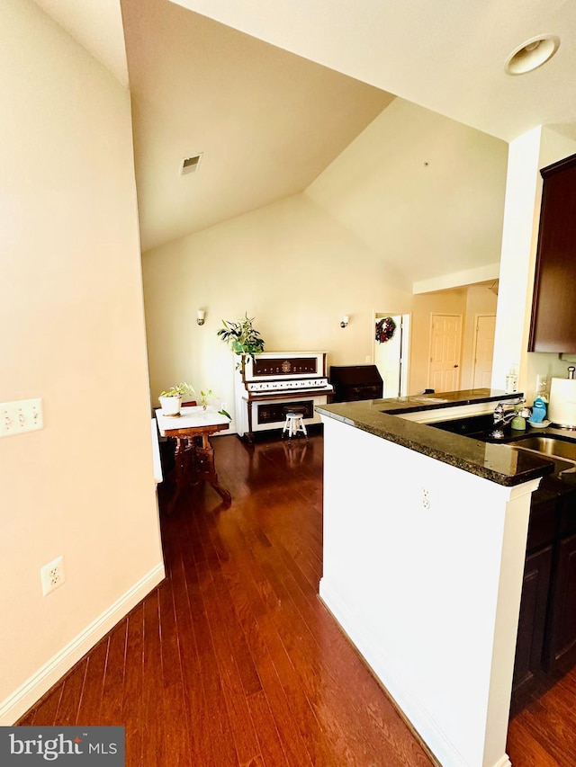 kitchen with dark brown cabinetry, dark hardwood / wood-style floors, kitchen peninsula, dark stone counters, and lofted ceiling