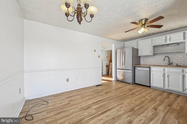 kitchen with stainless steel appliances, backsplash, white cabinetry, ceiling fan with notable chandelier, and sink