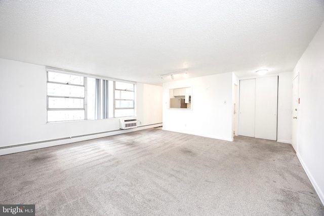 carpeted empty room featuring rail lighting, a textured ceiling, a wall unit AC, and a baseboard radiator