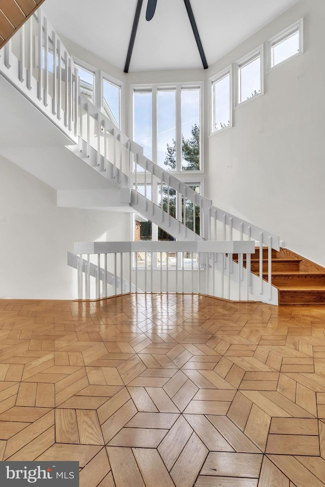 unfurnished living room featuring ceiling fan, a towering ceiling, and light parquet floors