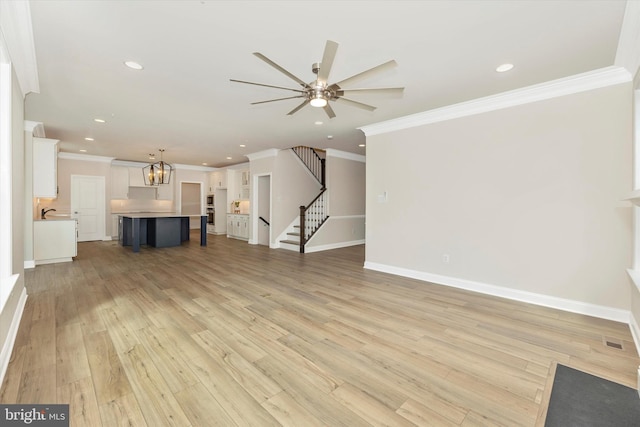 unfurnished living room featuring ceiling fan with notable chandelier, light hardwood / wood-style floors, and ornamental molding