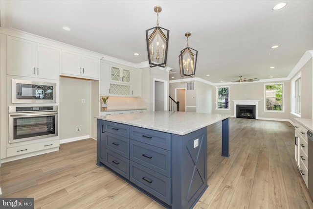 kitchen with stainless steel oven, ceiling fan with notable chandelier, built in microwave, decorative light fixtures, and white cabinetry