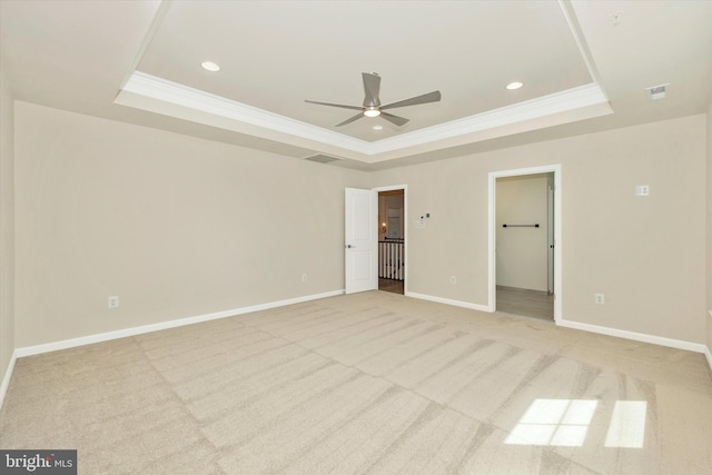 unfurnished bedroom featuring a raised ceiling, a walk in closet, crown molding, ceiling fan, and light colored carpet