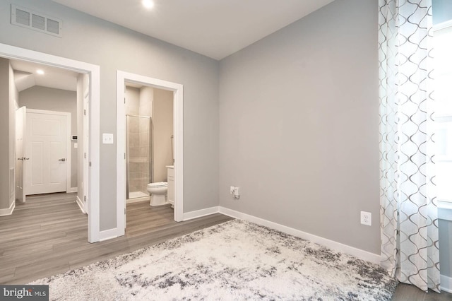 unfurnished bedroom with ensuite bathroom and wood-type flooring