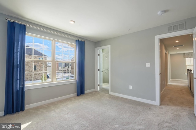 unfurnished bedroom with light colored carpet and a walk in closet