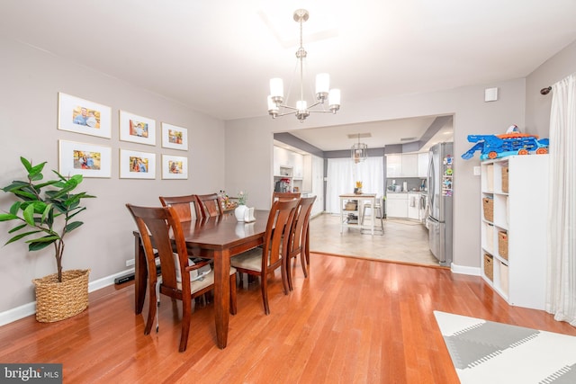 dining area with light wood-type flooring and an inviting chandelier