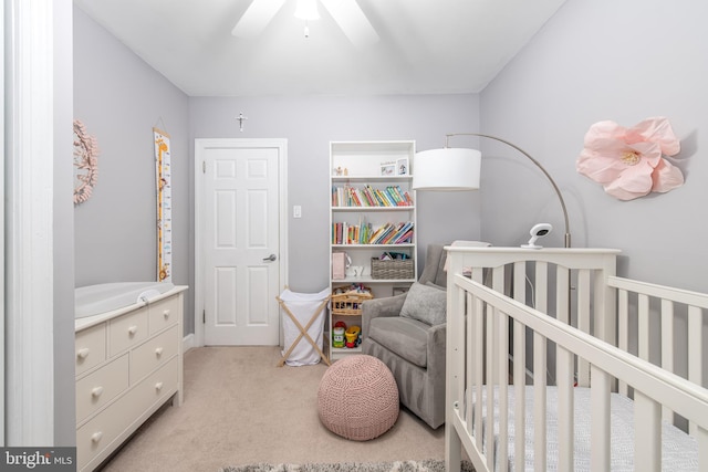 bedroom with ceiling fan, a nursery area, and light carpet