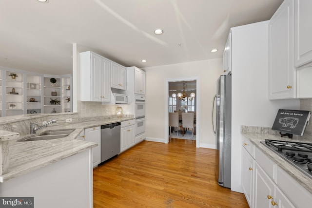 kitchen with light stone countertops, white cabinetry, sink, appliances with stainless steel finishes, and light wood-type flooring