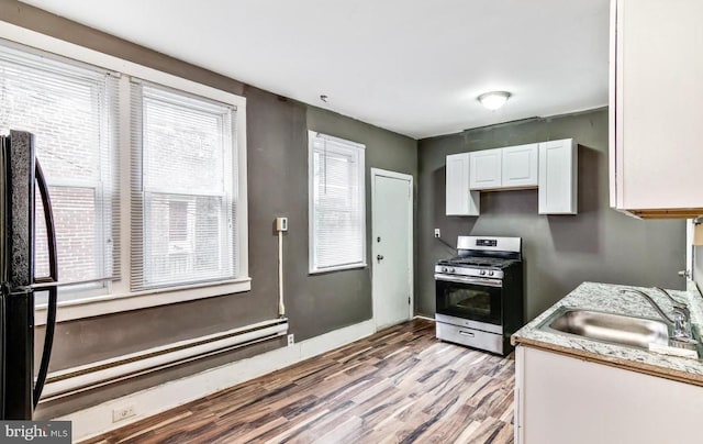 kitchen with sink, stainless steel gas range oven, white cabinetry, black fridge, and light hardwood / wood-style flooring