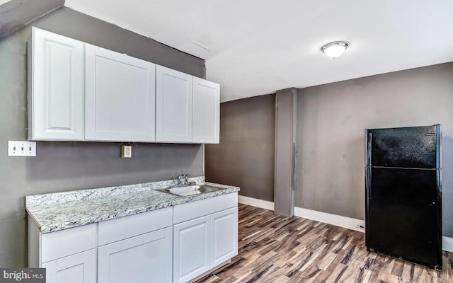 kitchen with sink, black fridge, white cabinetry, dark hardwood / wood-style floors, and light stone countertops