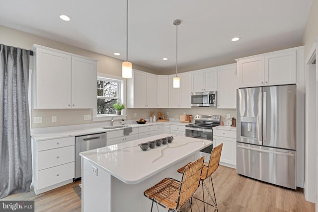 kitchen featuring a kitchen breakfast bar, stainless steel appliances, a kitchen island, decorative light fixtures, and white cabinetry