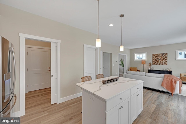 kitchen featuring a center island, white cabinets, hanging light fixtures, light hardwood / wood-style flooring, and stainless steel fridge