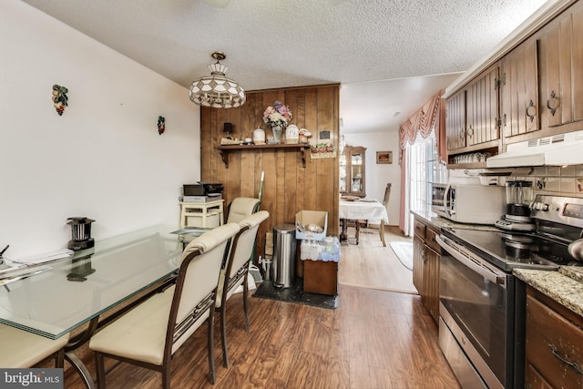 kitchen with wood walls, pendant lighting, stainless steel electric stove, a textured ceiling, and dark hardwood / wood-style flooring