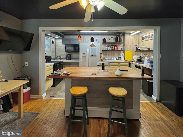 kitchen with a kitchen breakfast bar, tasteful backsplash, wooden counters, light hardwood / wood-style floors, and black appliances