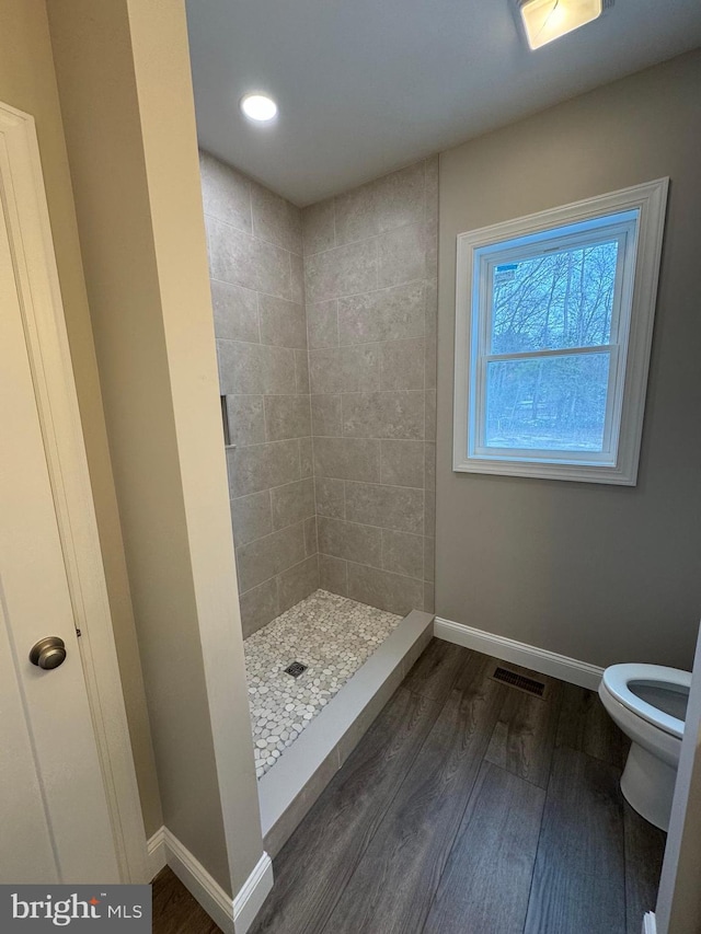 bathroom featuring toilet, wood-type flooring, and tiled shower